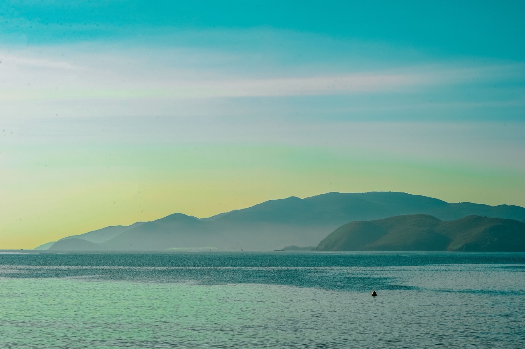 A calm sea below hazy mountains at first light